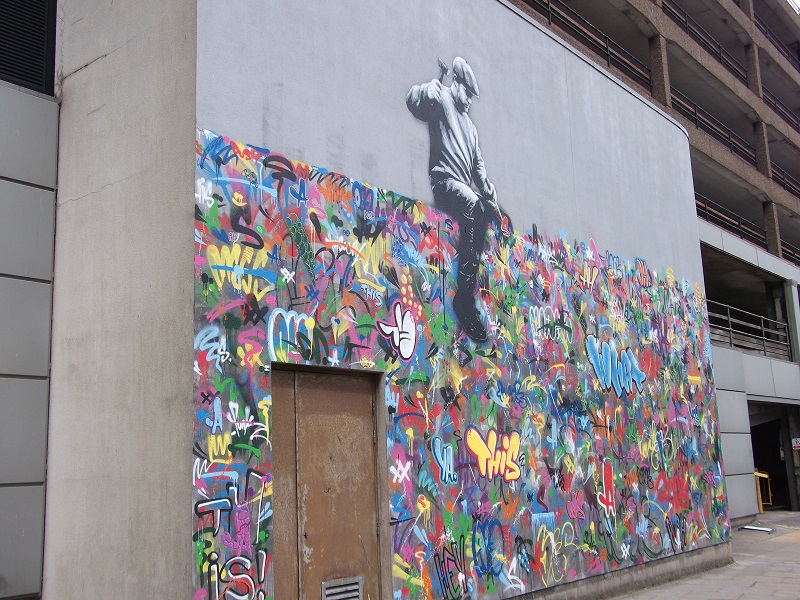 Street art by Martin Whatson, featuring a man on top of a wall of grafitti