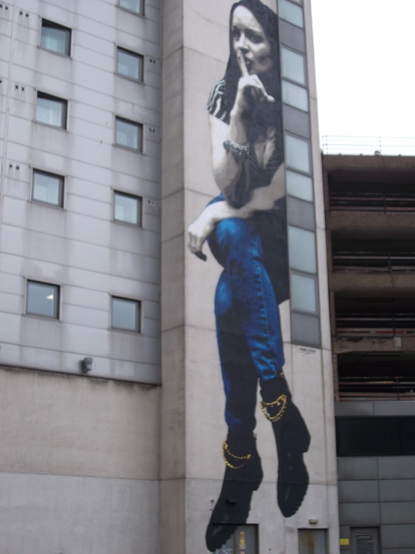 street art showing a girl in jeans placing a finger on her lips