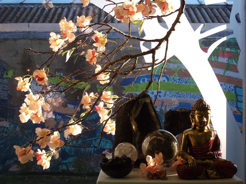 a tree branch with flowers and underneath crystal geodes, sphere and a Buddha ornament