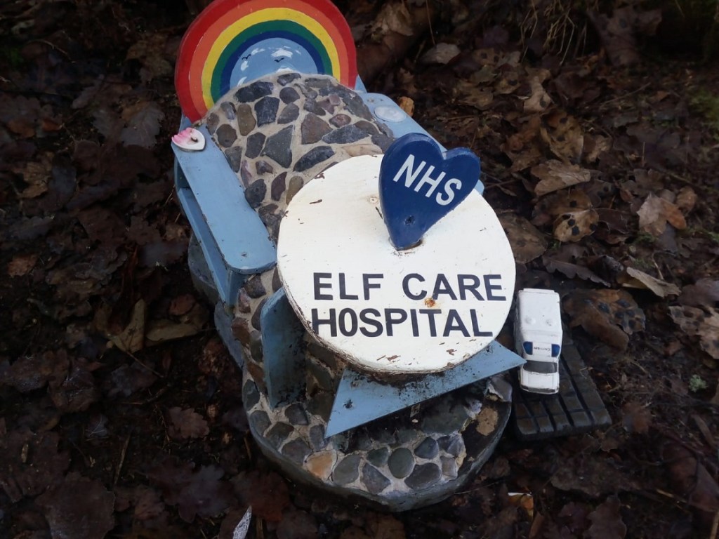 A wood and stone Elf Care Hospital structure with a toy ambulance next to it