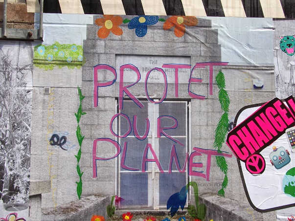 part of a street art mural, depicting the words Protect our Planet over a picture of a grey building with greenery and flowers painted on it.