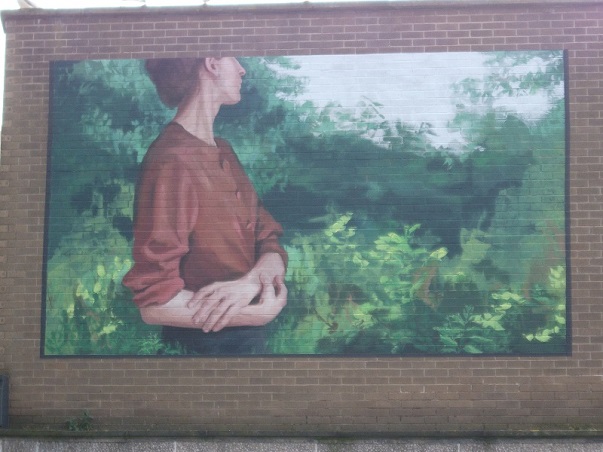 Street art showing a woman with folded arms gazing at the trees and green nature all around