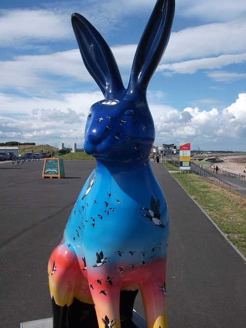 A hare sculpture with birds in flight painted on a background of sunset sky colours