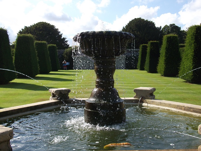 a fountain in front of sculpted hedge
