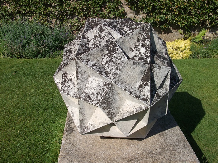 A grey stone sculpture of a multi-faceted cube