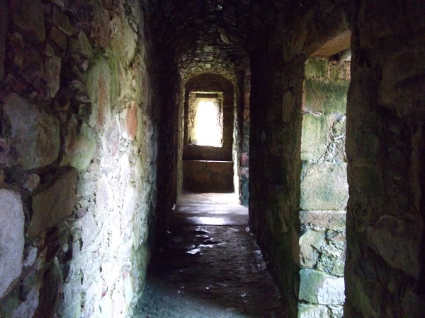 A narrow corridor surrounded by brick walls with a window at the end