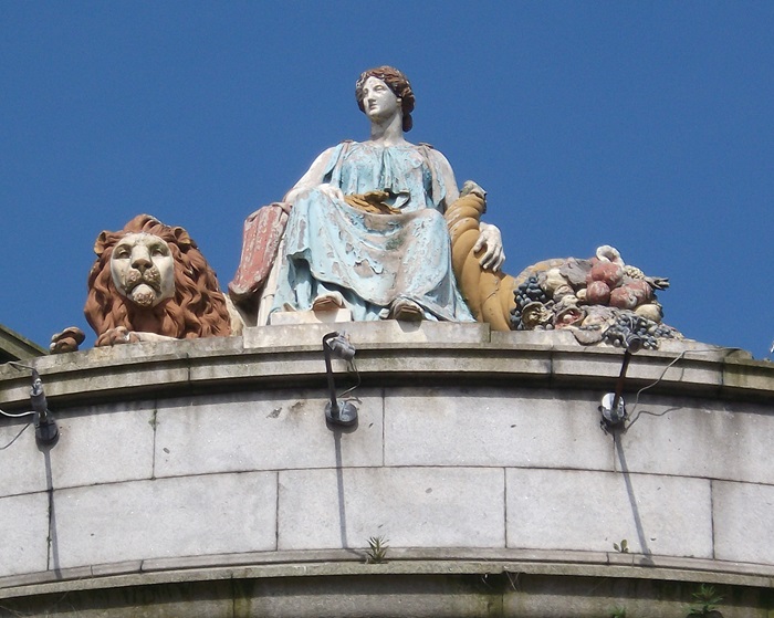 A statue of a woman in long flowing robes, with a lion at her feet and a cornucopia of fruit.