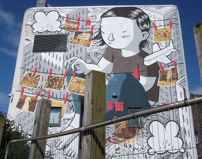 A girl arranging photographs on a washing line with buildings behind her
