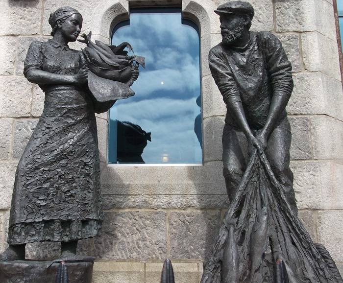 A bronze lifesize statue of a fisher woman and man with fish and a net