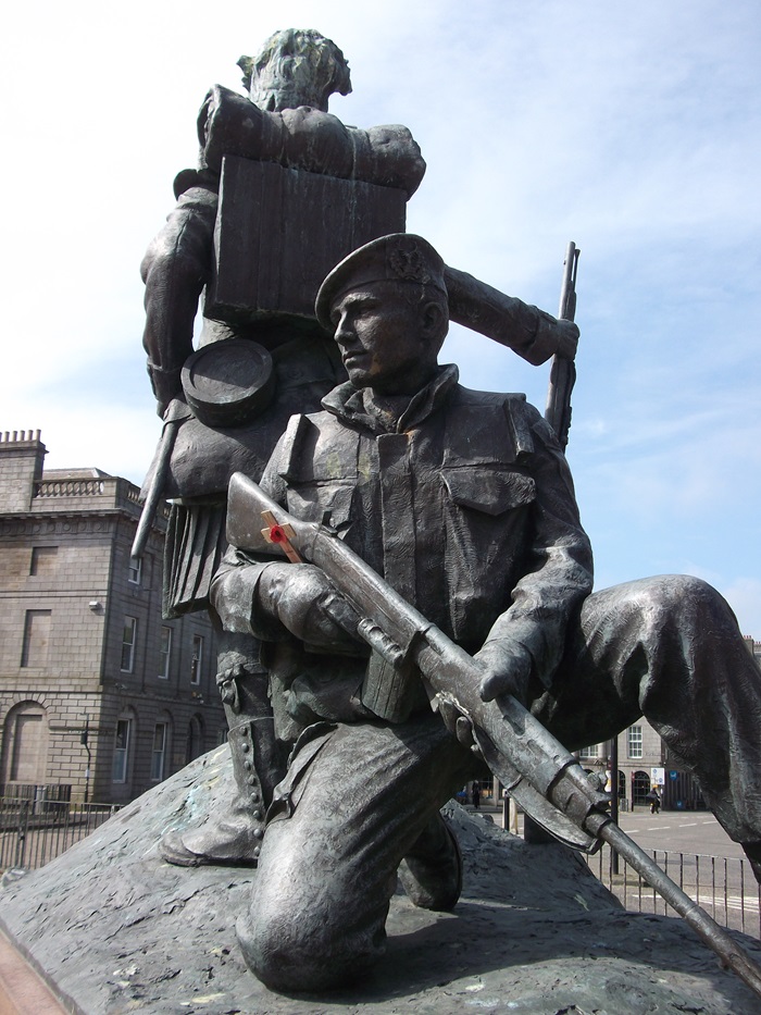 Two soldiers back to back, one is standing and one is kneeling.