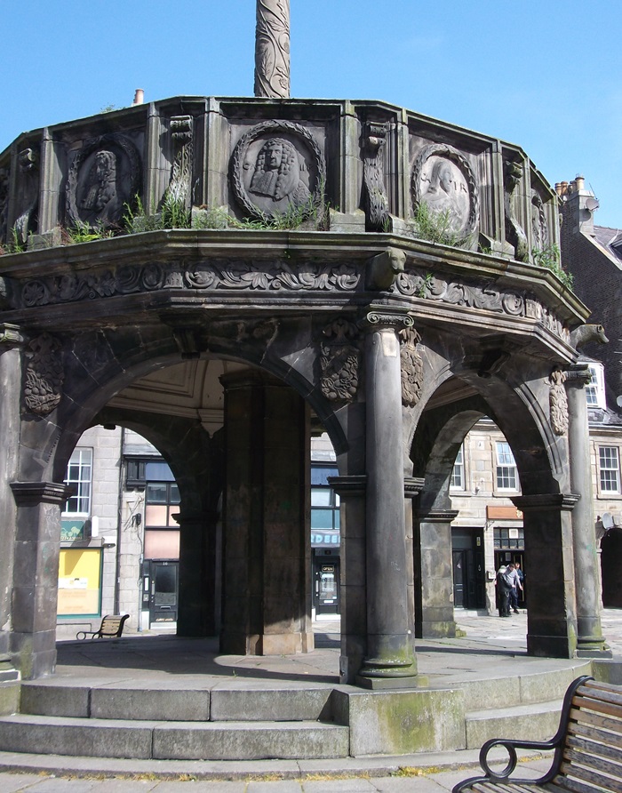a round stone market cross with stonework depicting Scottish monarchs