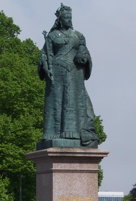 A grey statue of Queen Victoria in a long flowing dress holding a sceptre
