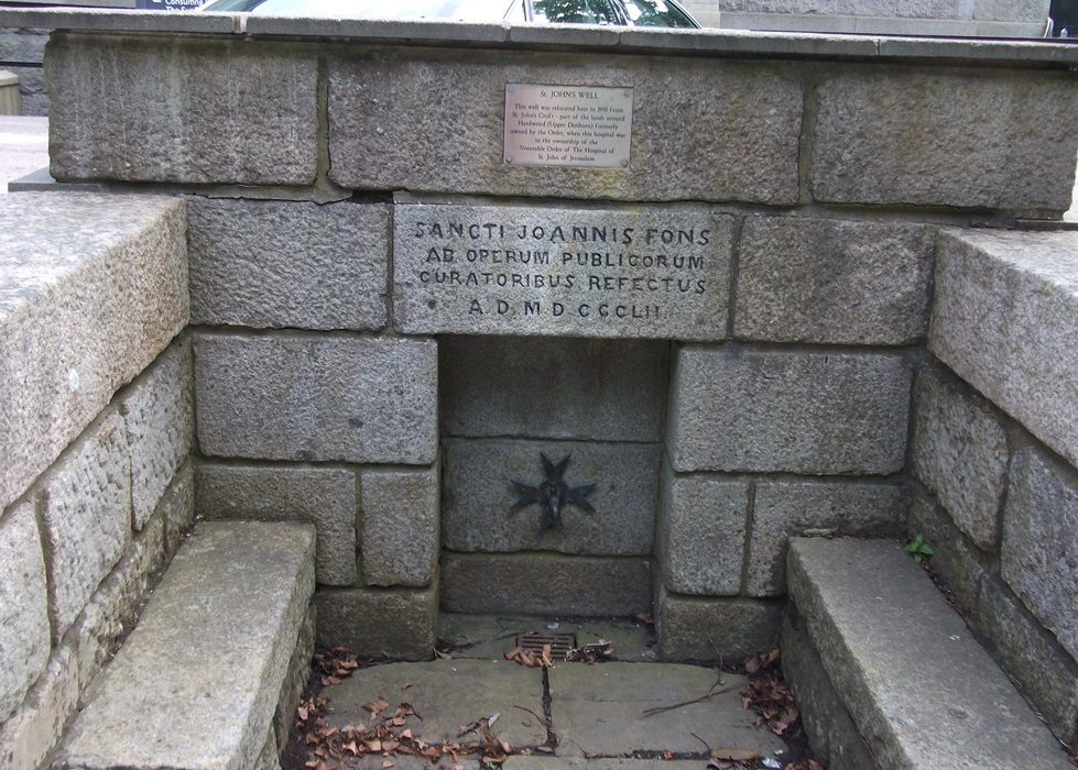 A low well surrounded by brick, with a knightly cross in the brickwork and an inscription in Latin.