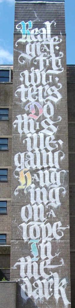 A block of words saying Real graffiti writers do this ... hanging on a rope in the dark