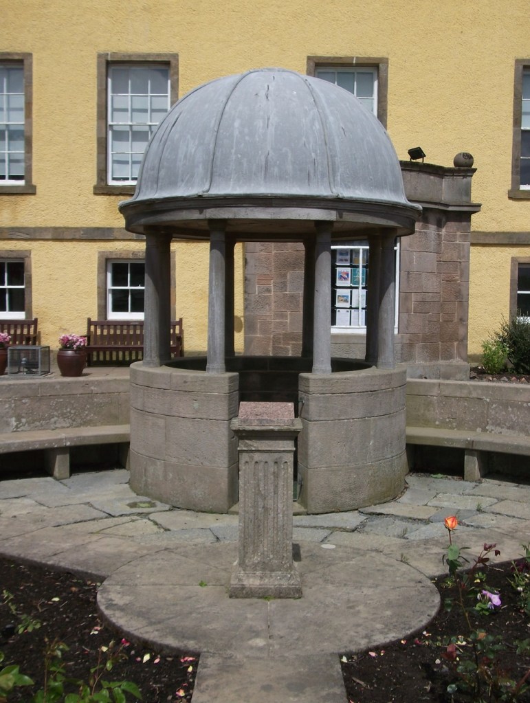 a grey monument in front of a yellow stately house