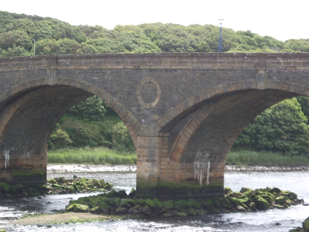 an arched bridge over a river with a green hill beyond