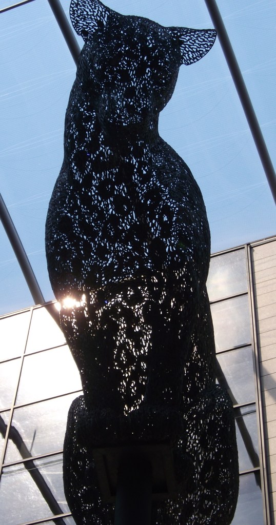 A metal sculpture of a seated leopard looking down.