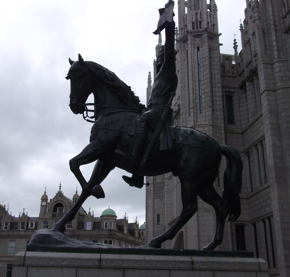 A statue of a man on a horse wearing a crown, with a sword at his side and holding up a parchment.