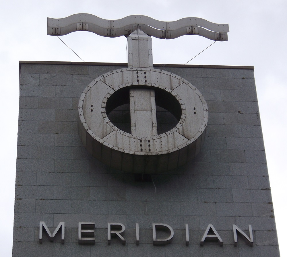 A metal sculpture of a circle  dissected by a vertical line with a wavy line above.