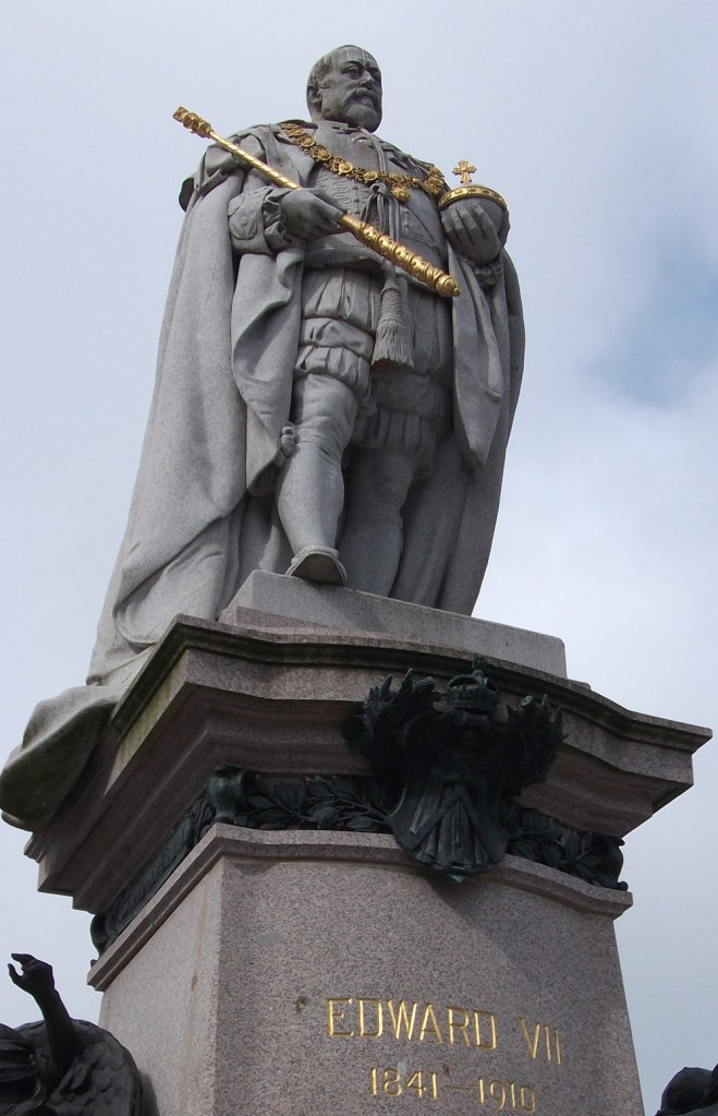 A stone statue of a king with golden sceptre and wearing long robes
