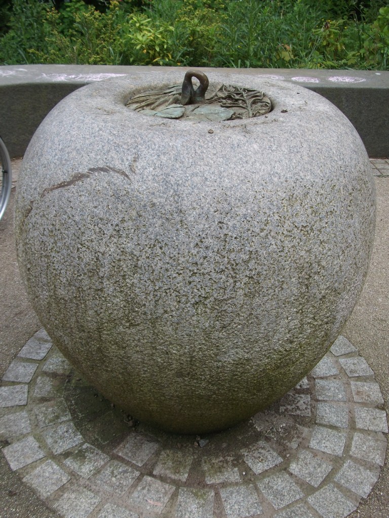A sculpture of an oval shaped traditional Nigerian water vessel, with a leaves feature on top