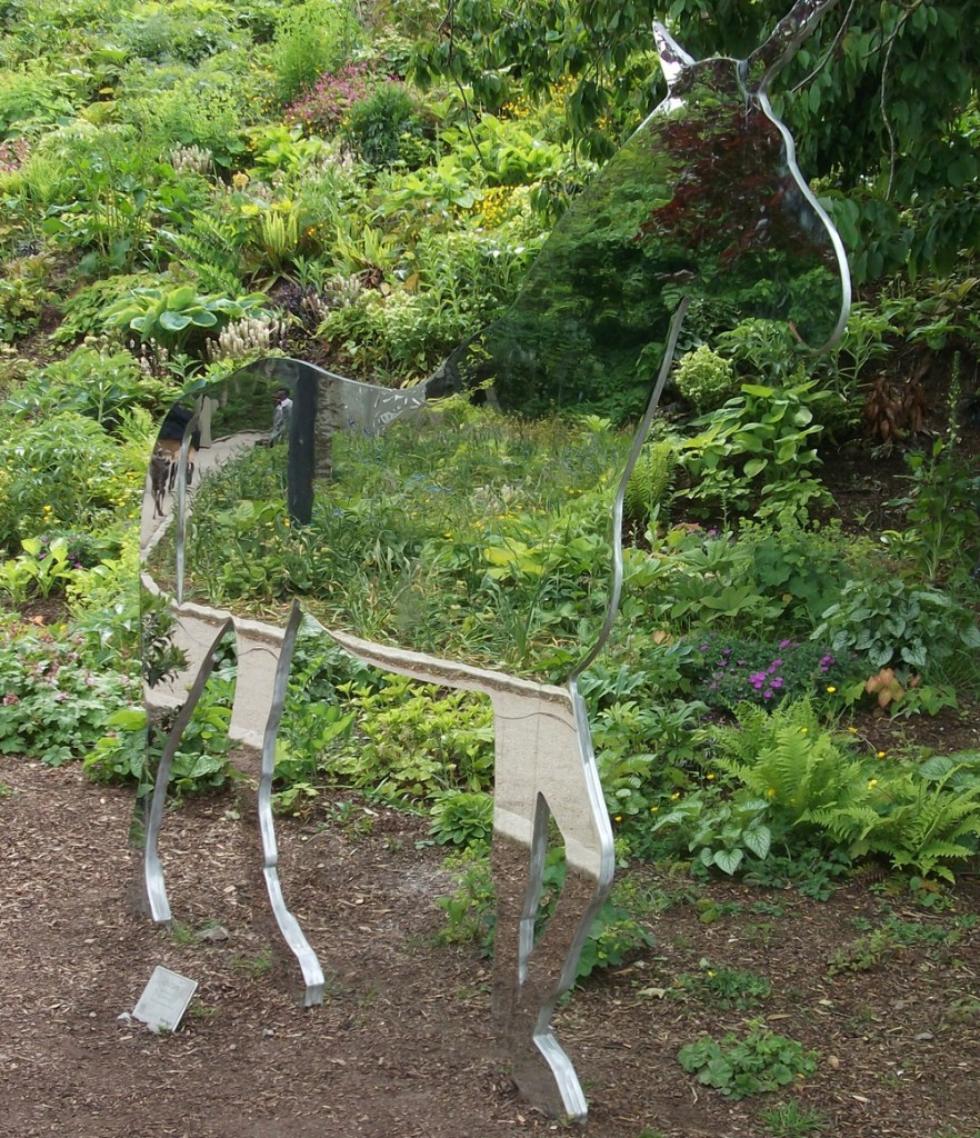 A mirror unicorn sculpture, with green shrubs behind.
