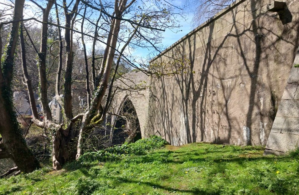 A stone bridge viewed from below with trees and grass in front of it