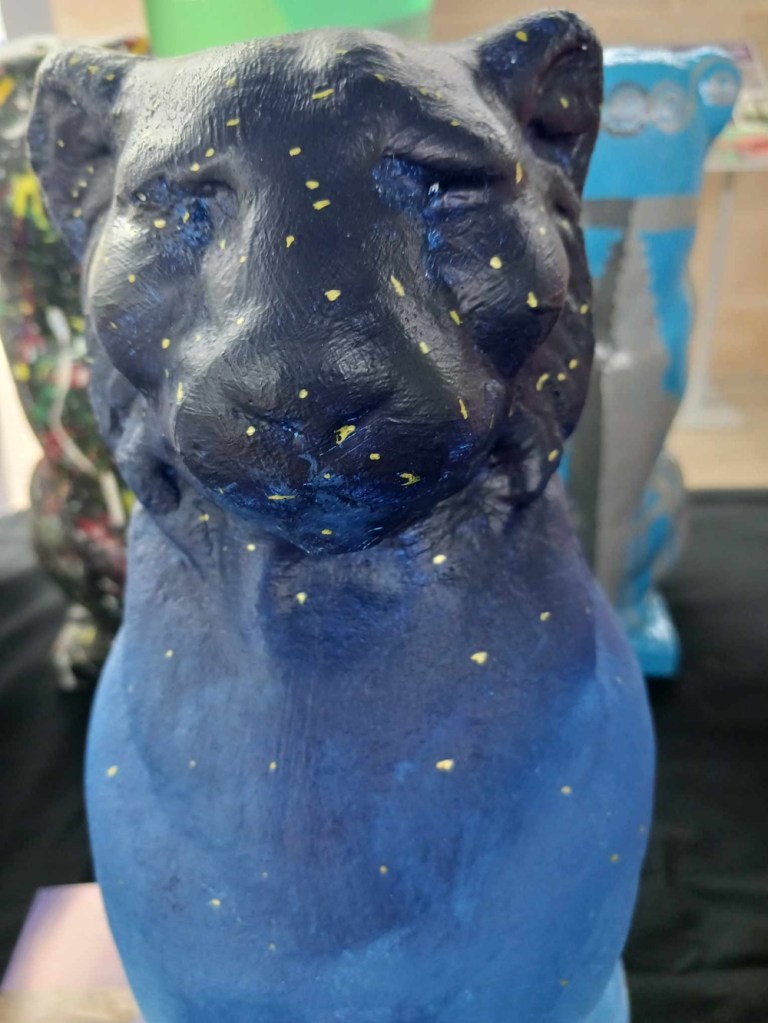 A blue cat statue with indigo blue head and lighter blue body with golden stars