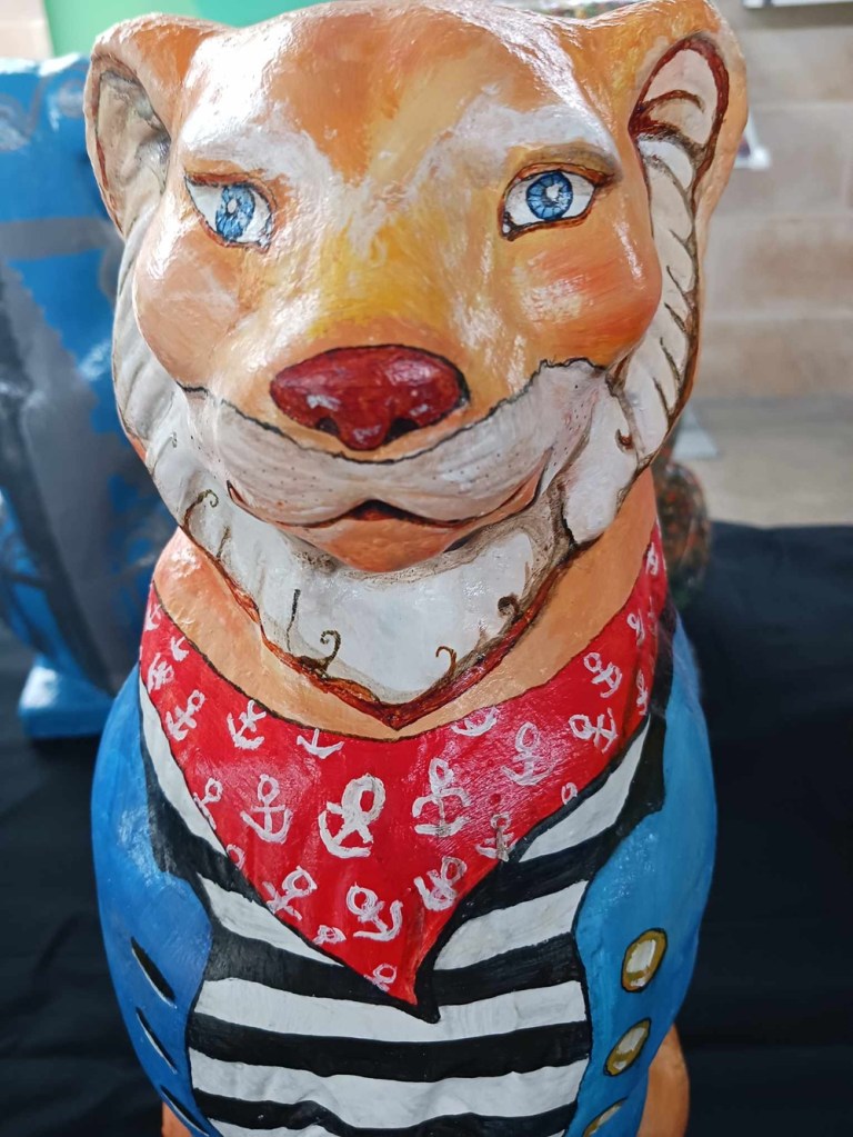 An orange cat statue with a white beard, red neckerchief, black and white striped shirt and blue coat