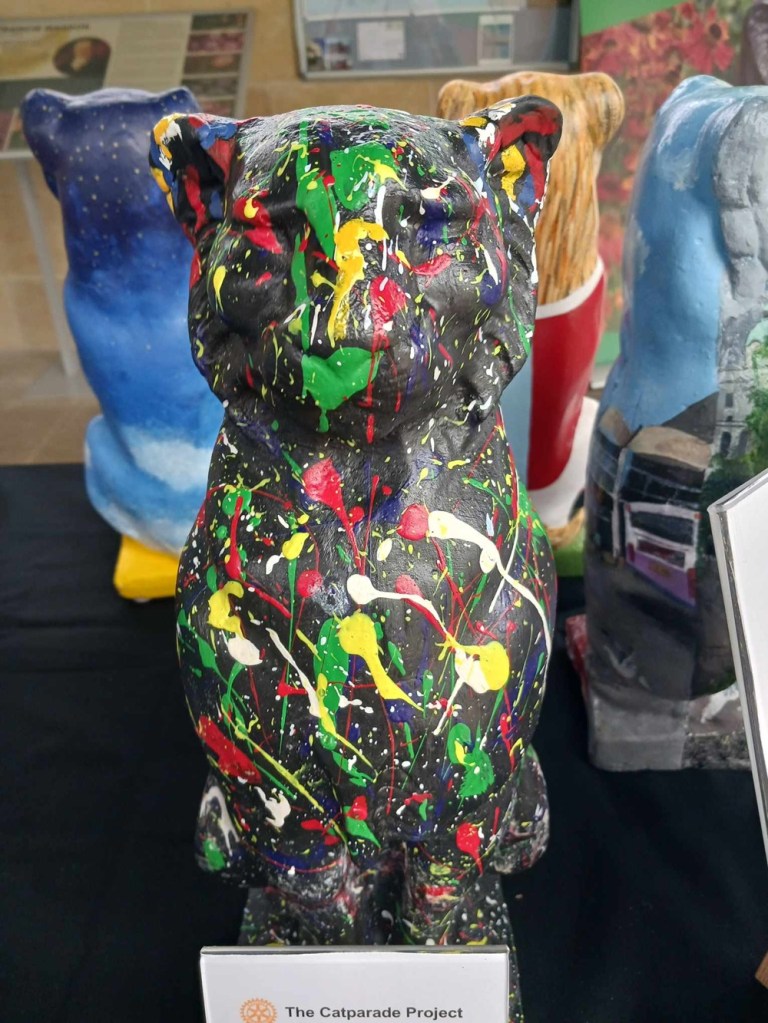 A grey cat statue with blotches of green, yellow, white and red paint