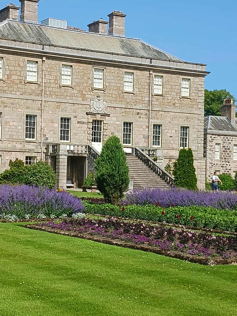 A stately brick mansion house with steps leading up to a door and six windows on each of the two stories above.