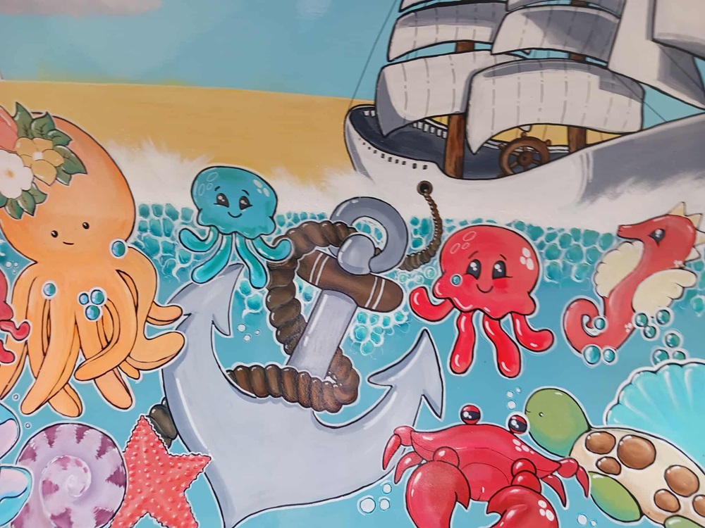 A painting of a ship and anchor surrounded by sea creatures including an octopus, crab, seahorse and jellyfish