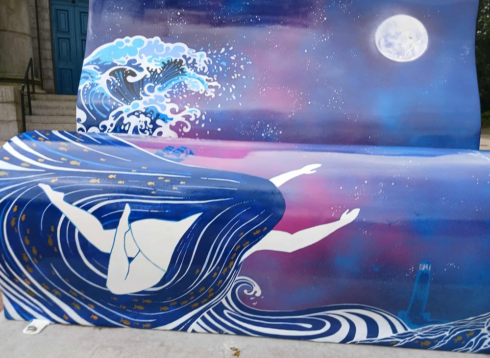 A blue and purple bench with a woman with very long hair swimming with waves around her and a moon overhead