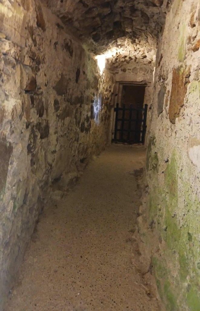A stone corridor with grilled doorway at end
