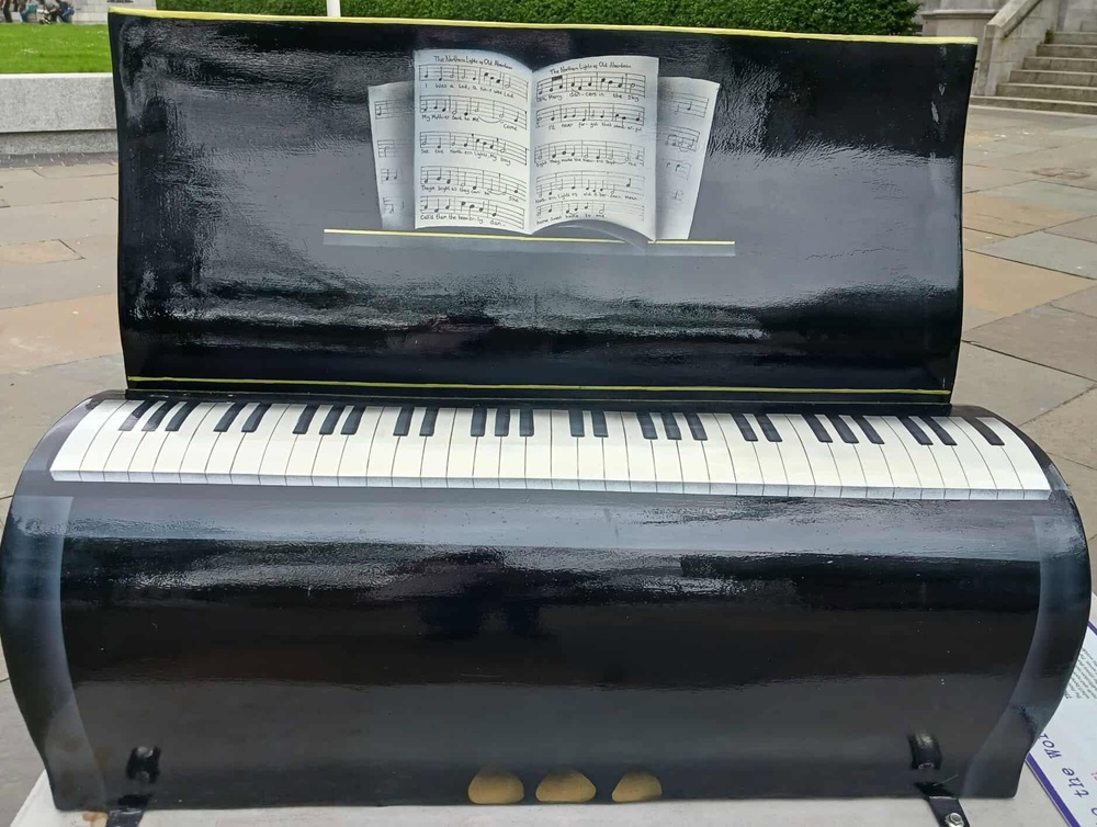 a bench painted to look like a black piano with music notes on a stand and black and white keys