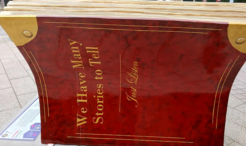 a deep red background with gold text stating We Have Many Stories to Tell ... Just Listen