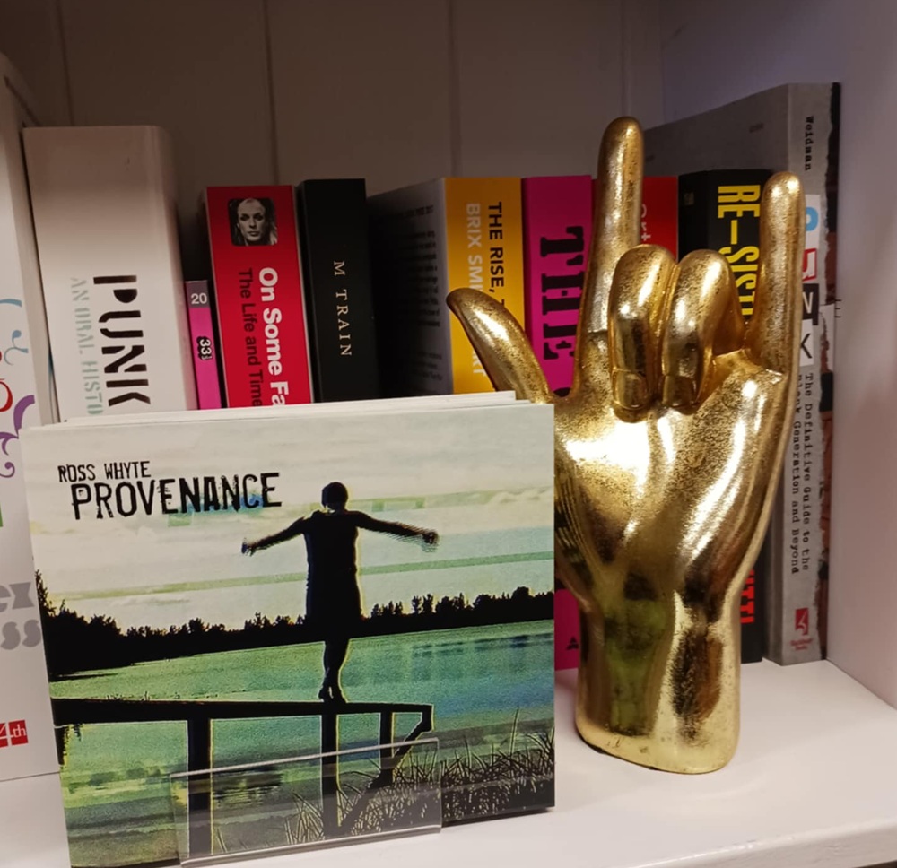 A golden hand ornament in front of book spines and next to a book cover of a woman walking down a fence at a lake