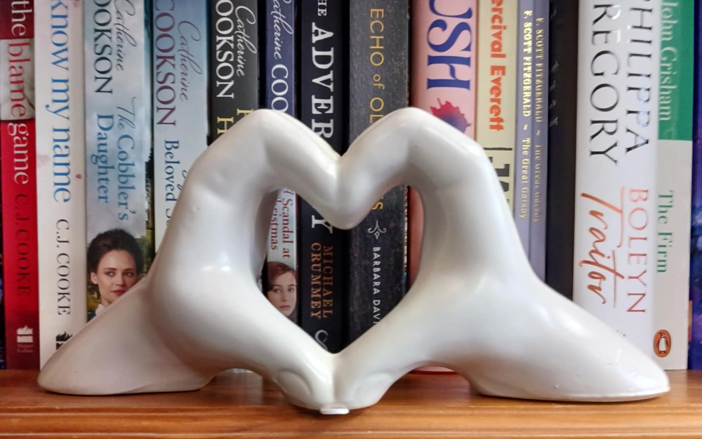 A white ornament of two hands touching making a heart shape in front of book spines