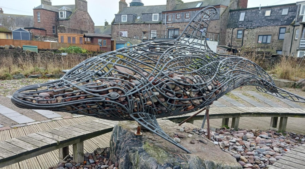 A grey metal sculpture of a dolphin with stones inside