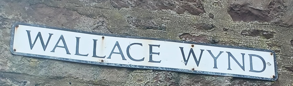 A white sign on a wall which reads Wallace Wynd

 