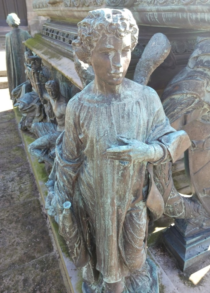 The sculpture of an angel with short curly hair, wings and flowing robes