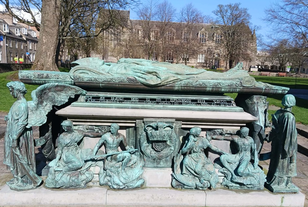 A soft green monument with the supine profile of a man on top and angels beneath