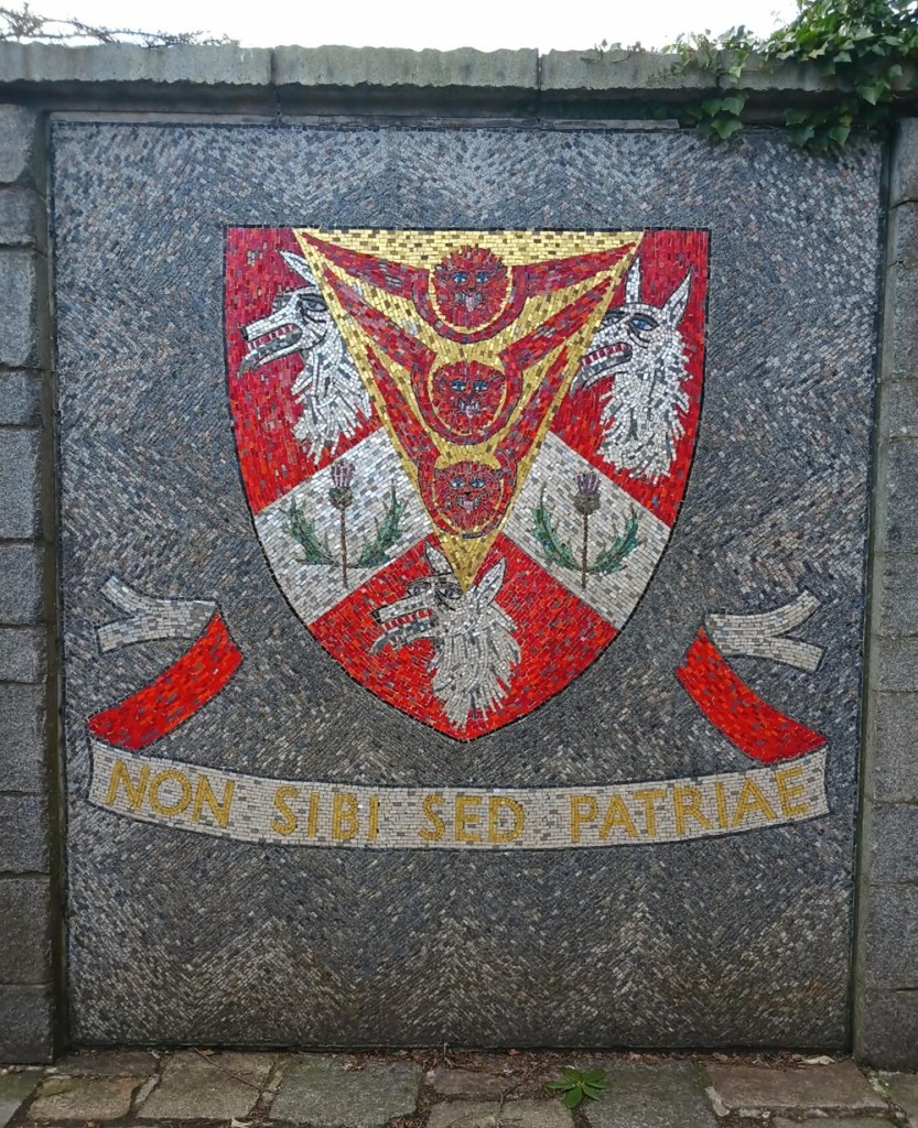 On a grey wall there is a painting of a red crest including three wolf heads, two thistles and three red animal heads with wings around them