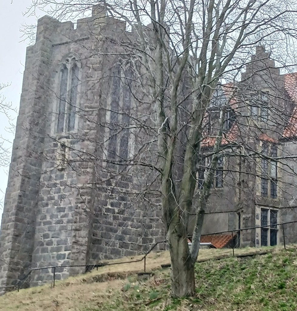 A large stone chapel with long ornate windows behind trees