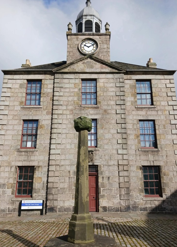 A three storey stone building with grid windows and a clock tower on top