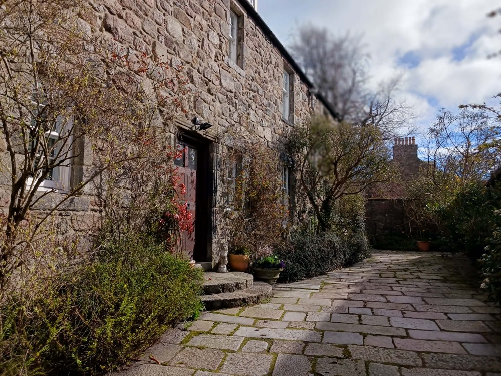 An old stone house with shrubs and trees against its walls
