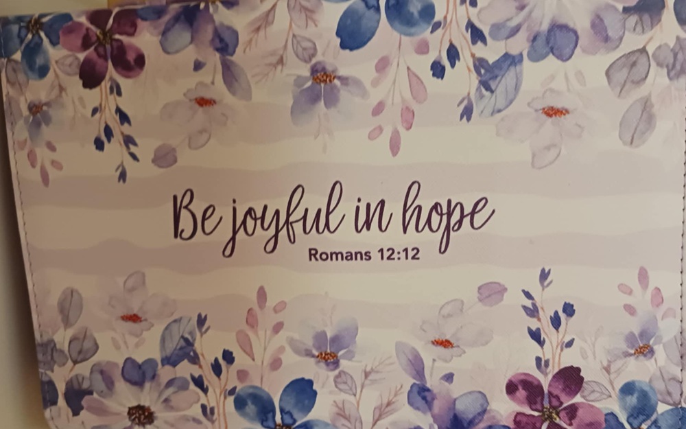 Be Joyful in Hope text on a pink background with blue flowers